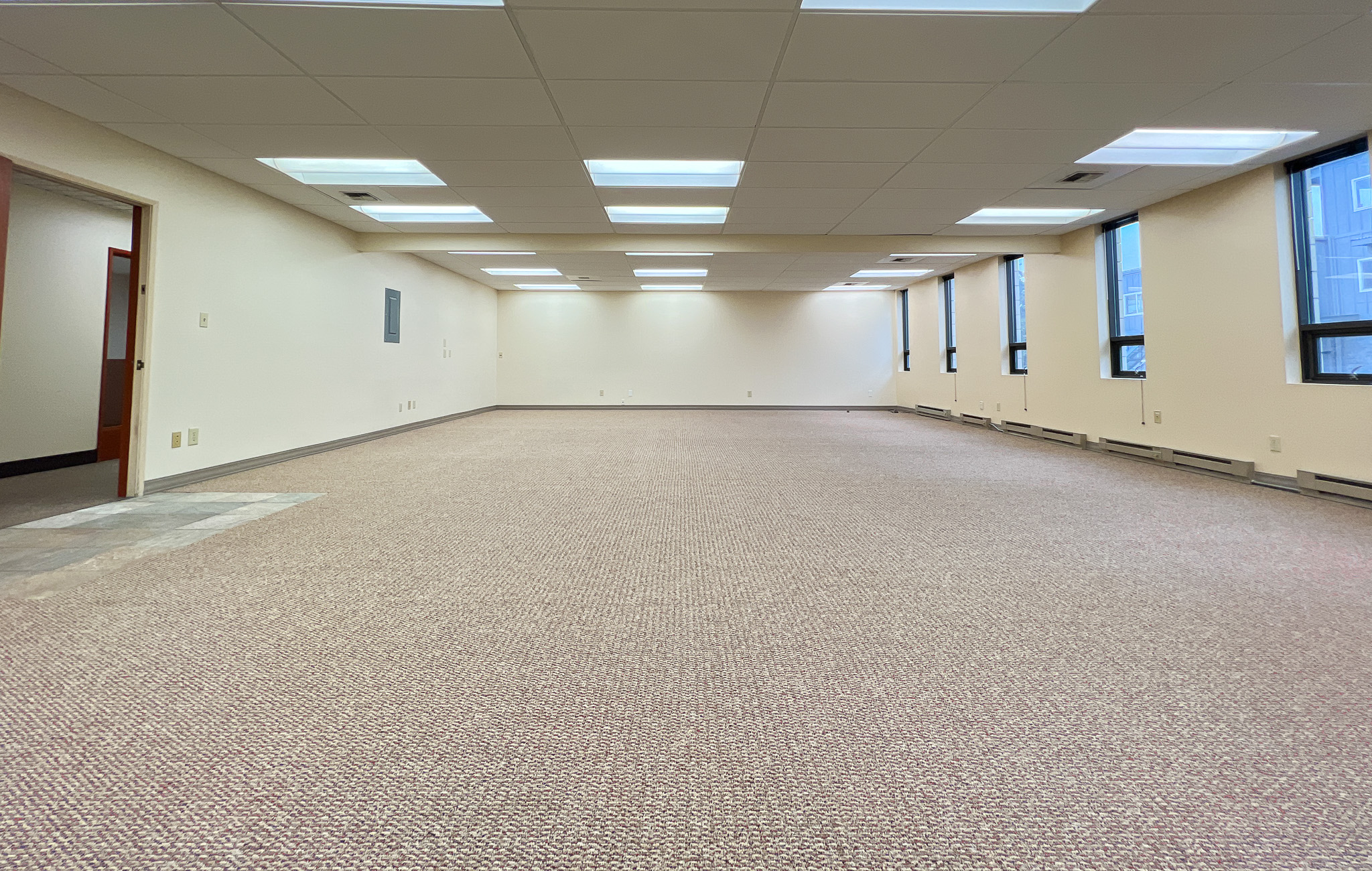 Interior of RSD Properties' Suite 102 in the 750 W 2nd Avenue office commercial office building in Anchorage, Alaska. Several windows on the right, tan carpeting and a drop ceiling with exit door on the left