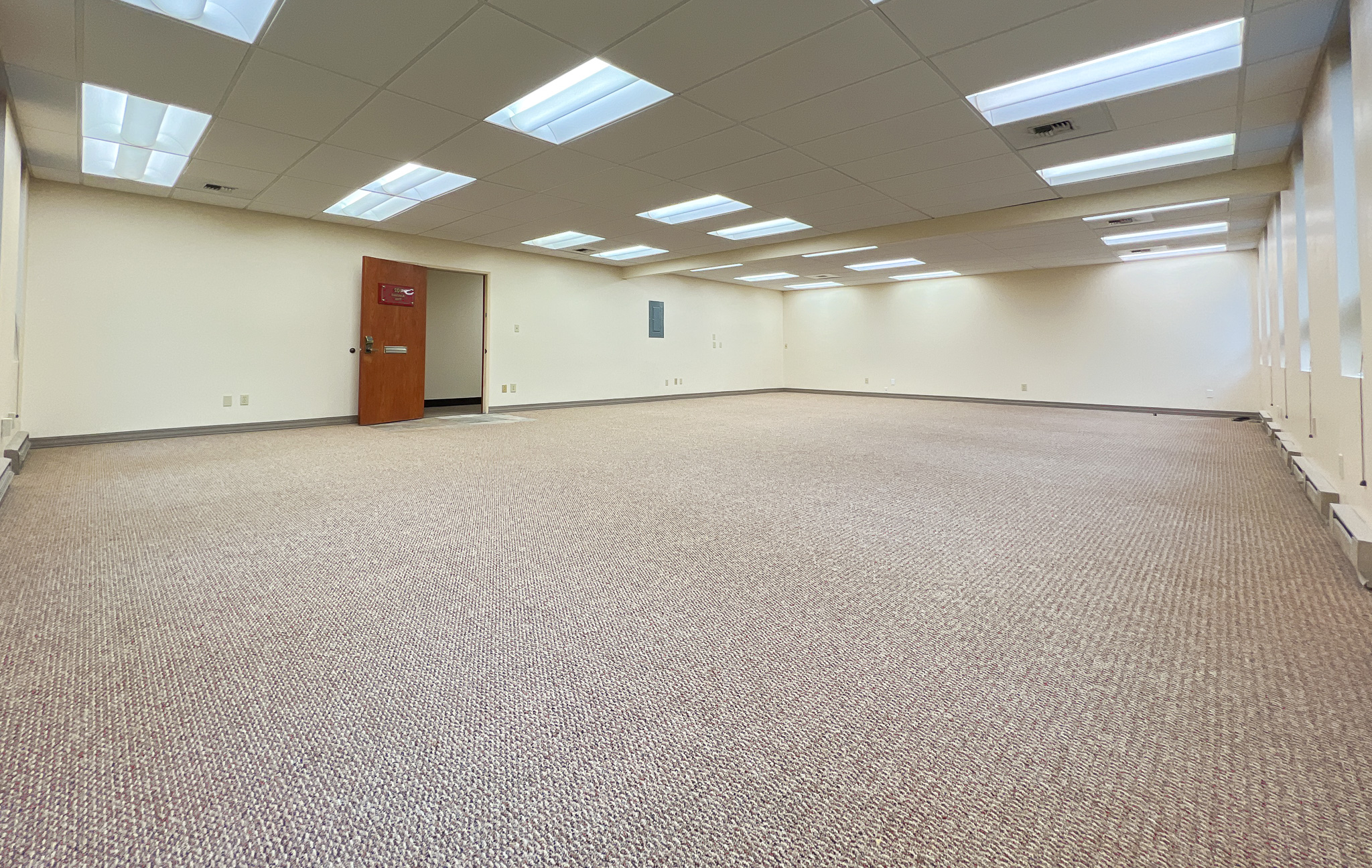 Interior of RSD Properties' Suite 102 in the 750 W 2nd Avenue office commercial office building in Anchorage, Alaska. Several windows on the right, tan carpeting and a drop ceiling, brown exit door on the left.