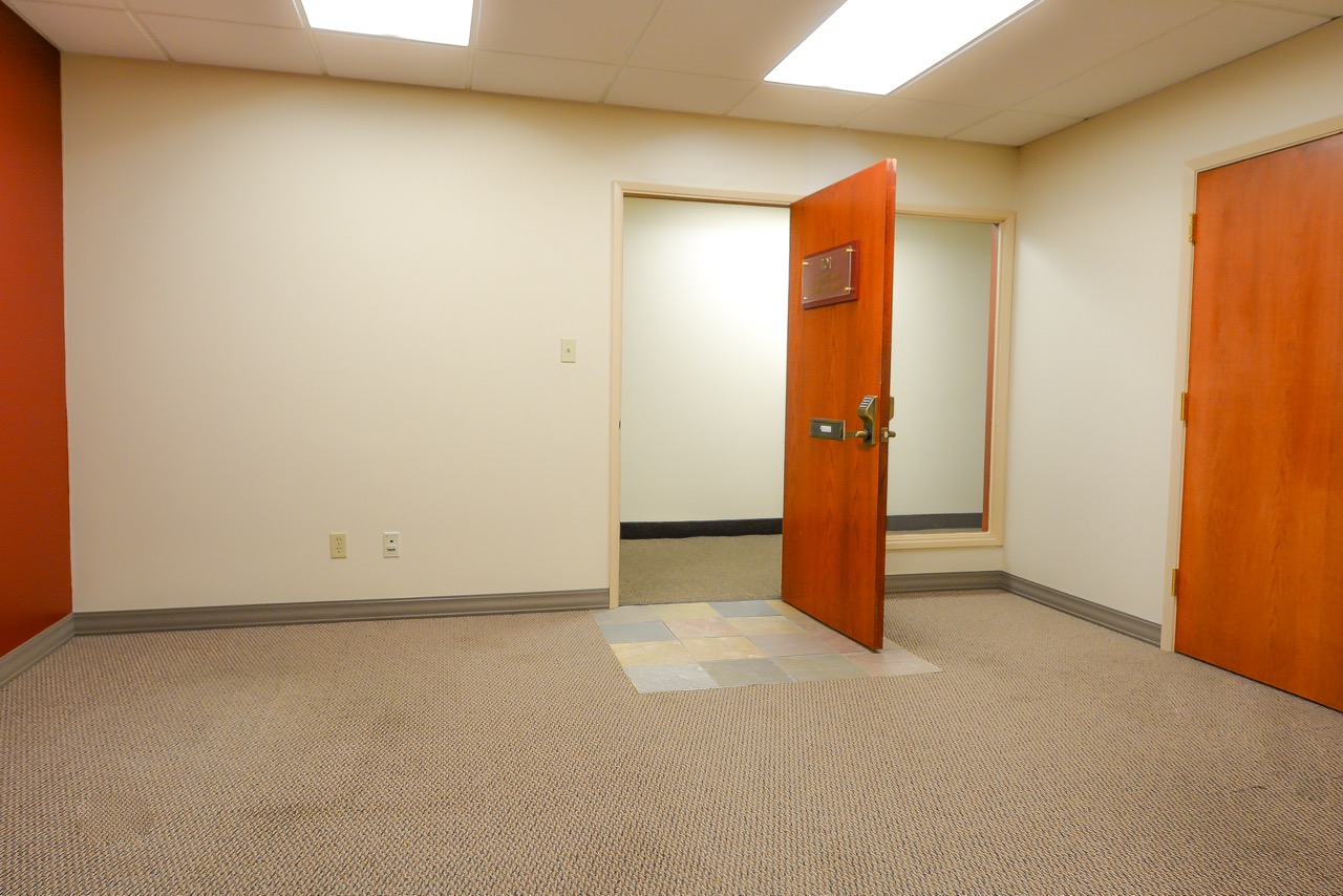 Interior of RSD Properties' Suite 101 at the 750 W 2nd Avenue commercial office building in Anchorage, Alaska. Tan walls and carpet with a brown exit door at center and large brown door on the right