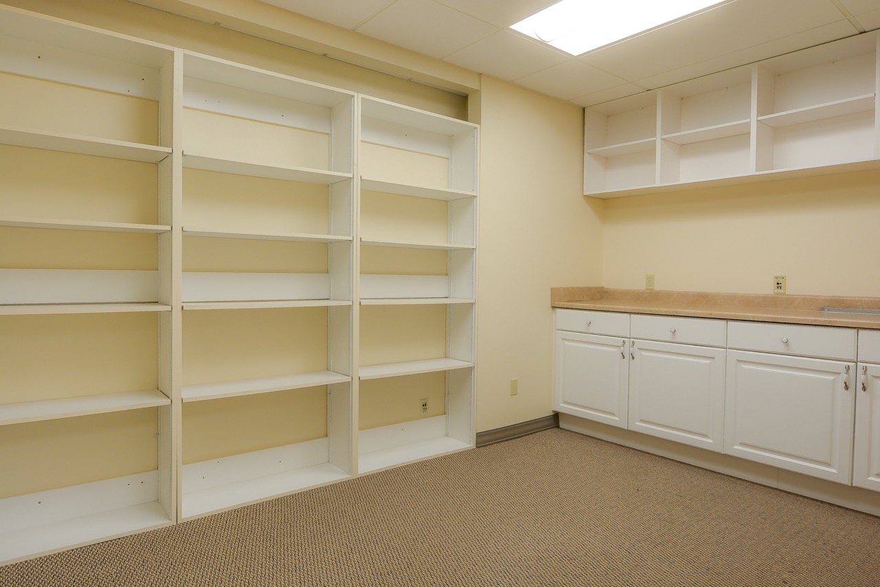 Interior of RSD Properties' Suite 101 in the 750 W 2nd Avenue commercial office building in Anchorage, Alaska. Tan room and carpet with built-in shelving on the left and shelves and storage counter on the right.
