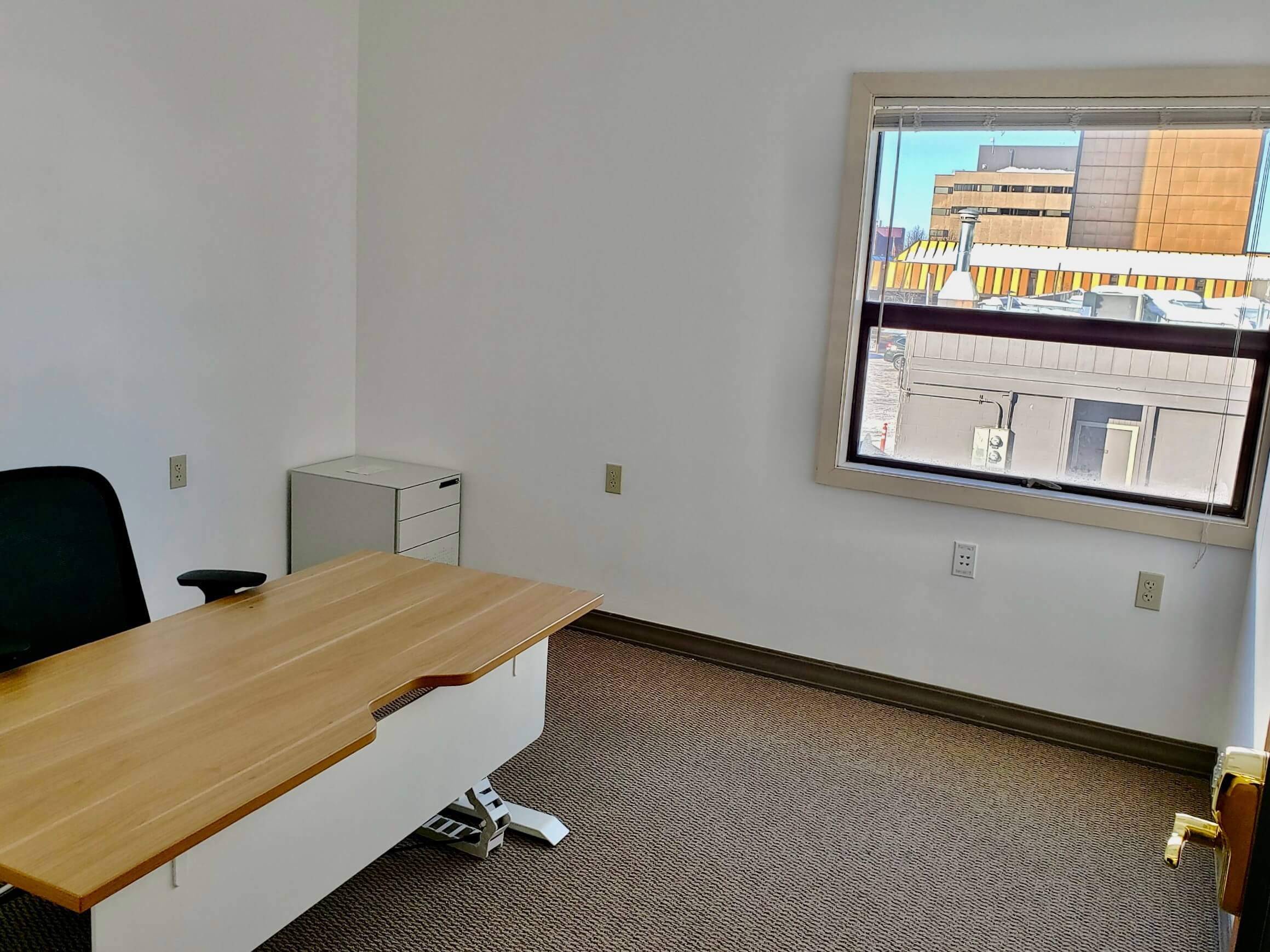 A coworking office at RSD Properties' Cowork By RSD Annex, with a desk, chair and filing cabinet on the left, and a window on the right showing a sunny Anchorage, Alaska day